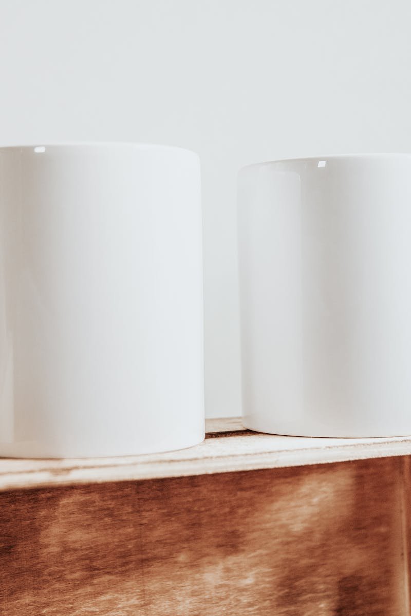 Two minimalist white ceramic mugs on a wooden box, perfect for coffee or tea.